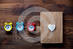 Three colorful alarm clocks and book with heart shape