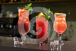 Three colorful cocktails in glasses on bar counter in pub or restaurant on bright blurred background. A lot of ice cubes and mint