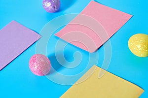 Three colorful eggs with glitters near blank square paper stickers lies on blue desk on kitchen