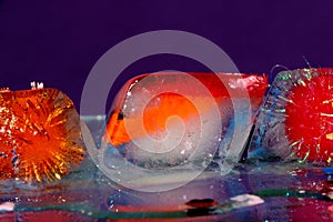 three colorful ice cubes on glass on a purple background