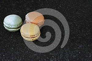 Three colorful macaroons are on the black background. Three tasty cookies