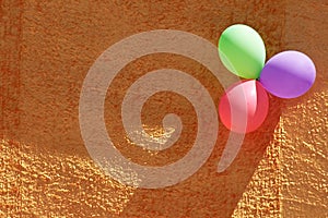 Three colorful party balloons and orange textured wall