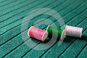 Three colorful sewing threads laying on green textile background - Image