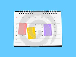 three colorful sticky notes attached on desk calendar isolated on blue