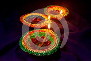 Three colorful terracotta oil lamp or diya lit during diwali on blue cloth background