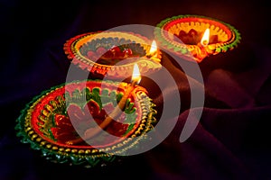 Three colorful terracotta oil lamp or diya lit during diwali on blue cloth background