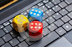 Three colorful wooden game dice showing six laying on a modern laptop keyboard. Lots of dice showing six, winning, lucky number