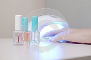 Three colorless transparent nail polish bottles in background of female hands in gel uv led nail white lamp for drying manicure
