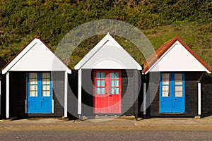 Three colourful beach huts with blue and red doors in a row