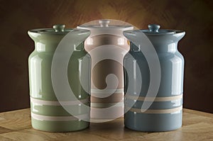 Three colourful ceramic canisters on timber bench with rustic background