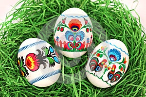 Three Colourful Easter Eggs with floral and roosters folk art pattern printed on stickers, in green paper grass nest.