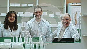Three competent pharmacists laughing in a pharmacy looking at camera