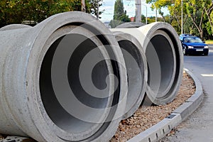 Three concrete pipes lie on the unfinished sidewalk near the road at the site of the road construction works in the city