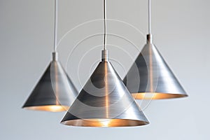 Three cone-shaped brushed steel pendant lights in a row, emitting a soft, warm glow