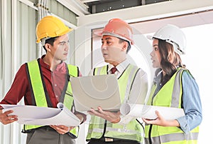 Three confident construction team, a female architect and two male engineers, wearing safety helmets,holding computer and blue