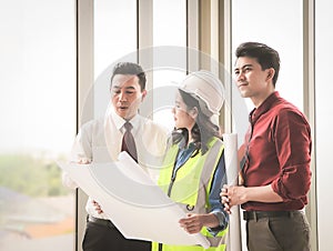 Three construction workers, one woman and two men standing by windows , holding blue print and  discussing about  project