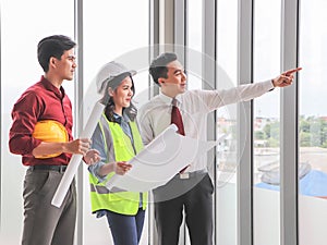 Three construction workers, one woman and two men standing by windows , holding blue print and  discussing about  project.Business