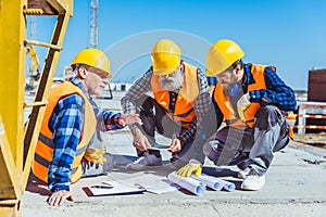 Three construction workers sitting on concrete at construction site, discussing