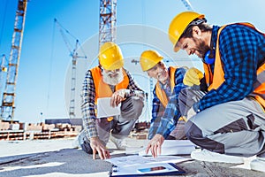 Three construction workers sitting on concrete at construction site, discussing