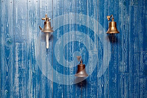 Three copper old vintage bells, doorbell, rope on a wooden blue aged wall. Concept decor element in interior of deck, cabin of