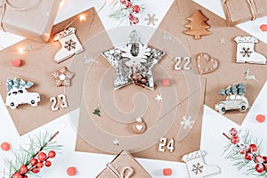 Three craft envelopes with wooden numbers 22,23,24, christmas decoration cookies and gifts lie on a white background.