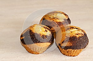 Three cupcakes with chocolate dousing on a wooden table