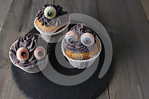 Three cupcakes with grey black cream and eyes. Halloween Holiday Preparation Concept