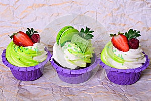 Three cupcakes with whipped cream, chocolate bar, strawberry ,decorated macaroons on crumpled paper. Picture for a menu or a