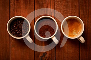 Three cups of espresso, freshly ground coffee and coffee beans on a wooden table