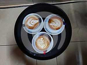 Three cups of hot cappuccino coffee served on a black tray