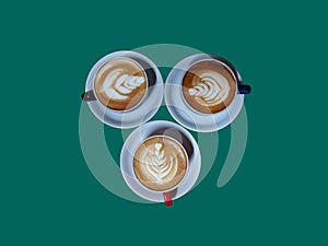 three cups of hot cappuccino coffee on a teal background