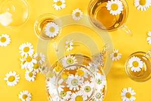 Three cups of tea and transparent teapot with camomile flowers on yellow background. Chamomile Tea Benefits Your Health concept.