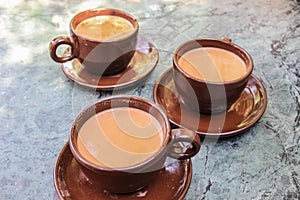 Three cups of traditional Nepalese tea with milk and spices in brown ceramic cups