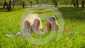 Three cute blond girls are sitting on lawn in garden under vintage sun umbrella