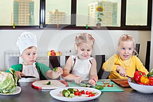 Three cute kids are preparing a salad in the kitchen