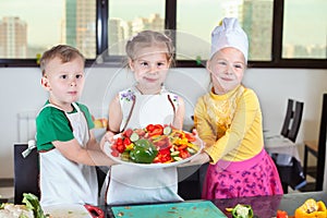 Three cute kids are preparing a salad in the kitchen