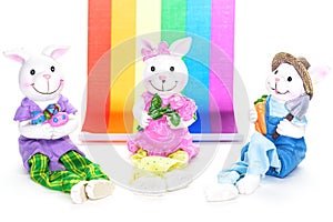 Three cute porcelain bunny rabbits ready for the Easter holiday, in front of a rainbow flag