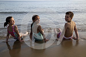 Three cute preteen children sitting in the water on the beach