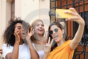 Three cute young girls friends having fun together, taking a selfie at the city