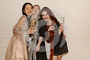 Three cute young interracial girls celebrate new year with champagne on white background.