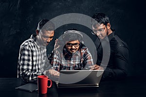 Three dark-skinned guys are chatting in the laptop wearing headphones