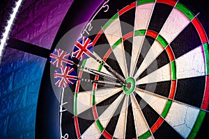 Three darts with uk flag flights in triple double bullseye on professional sisal steeldart board in colorful LED illumination on