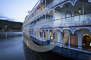 Three-deck cruise ship with lights in the cabins moored at the pier on the Columbia River
