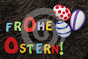 Three decorated Easter eggs and colorful letters saying `Happy Easter` in German on brown shag.