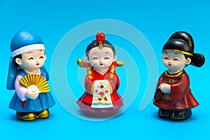 Three decorative ceramic Korean figures in traditional colorful clothes Han bock Figures are allocated over a turquoise background