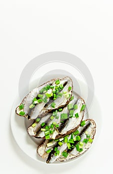 Three delicious sandwiches with rye bread, butter, small salted fish and green onions on a white plate, white space