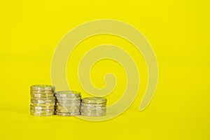 Three Descending Stacks of UK GBP Sterling One Pound Coins on a Yellow Background.