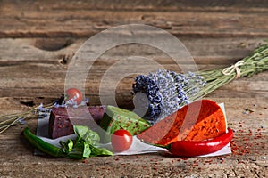 Three different colored gourmet cheeses lying on rough wooden planks with vegetables, copy space above