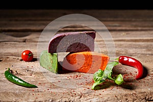 Three different colored gourmet cheeses lying on rough wooden planks with vegetables, copy space above