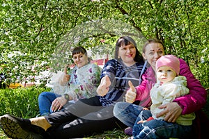 Three different funny women and one small seriously girl in the park full of apple blossom trees in a spring day. Aunts and niece